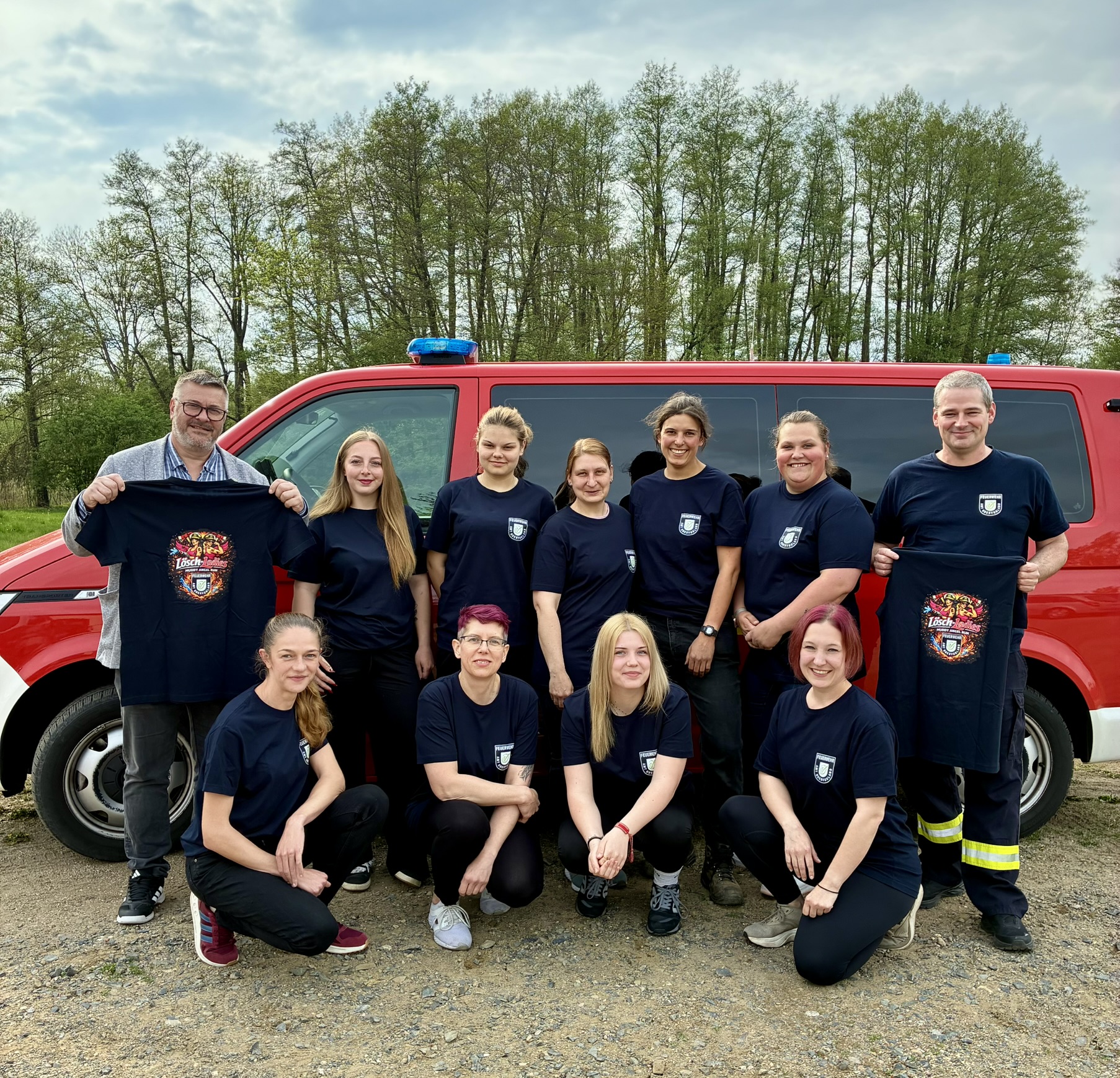 Bild zur Meldung: Feuerwehrfrauen als „Lösch-Ladies“ beim Muddy Angel Run. Auf dem Bild sind der Amtsdirektor Meyer, der Amtswehrführer Erben sowie mehrere Kameradinnen aus den Feuerwehren des Amtes Odervorland vor einem Mannschaftstransportwagen der Feuerwehr zu sehen. Es werden T-Shirts gezeigt, welche gespendet wurden.